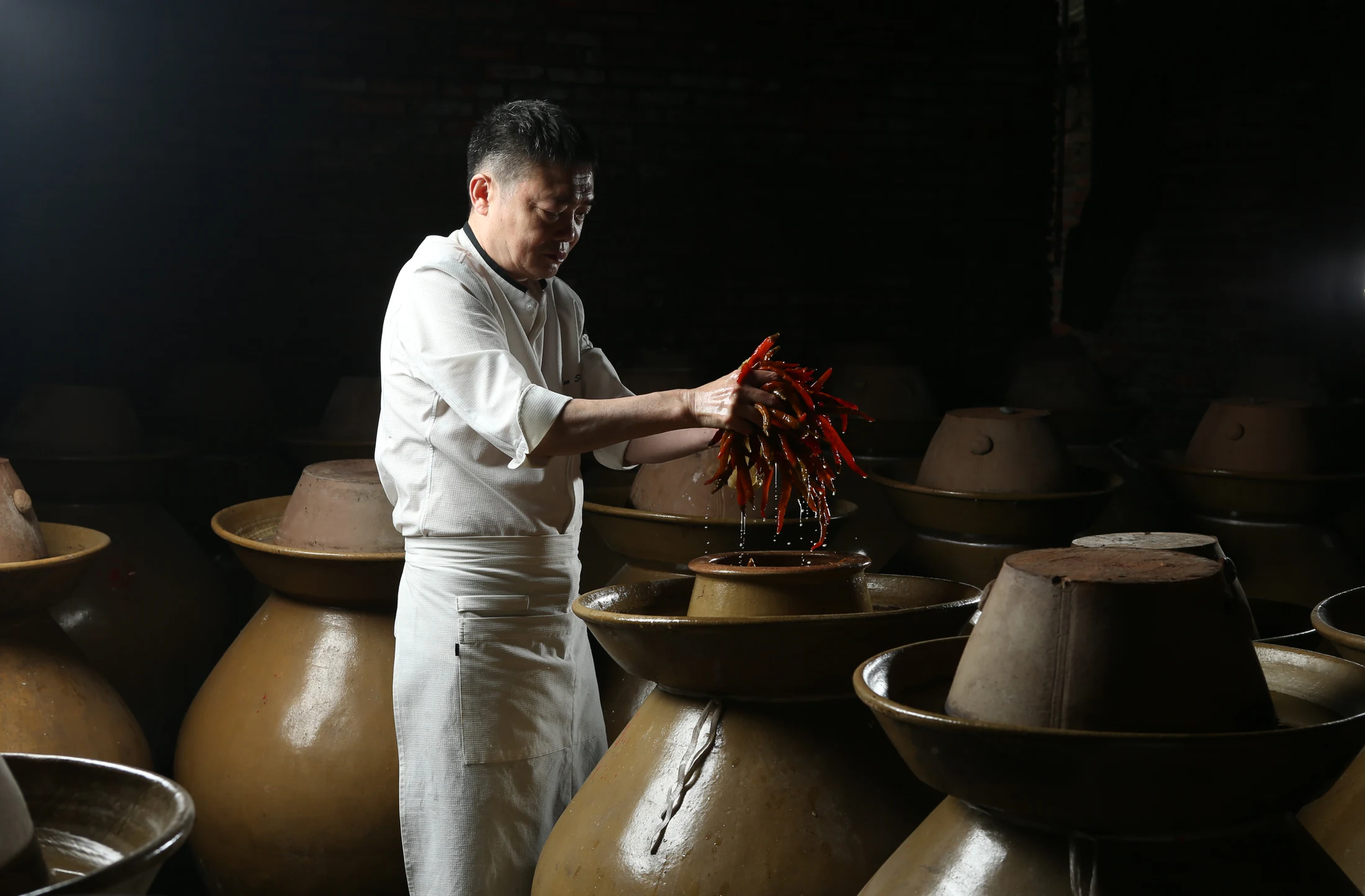 Chef Lam Shan handling fermented ingredients among traditional clay jars